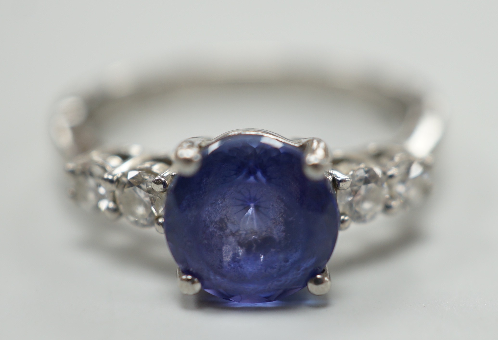 A modern Illiana platinum, single stone round cut tanzanite and four stone diamond set dress ring, size O, gross weight 5.7 grams.